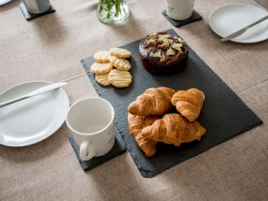 A table with croissants, cookies, a chocolate cake, mugs, plates, and knives at Wall Cottage in Burford