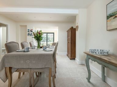 A dining room with a table set with cups plates and flowers a wooden cabinet and a side table with a tray at Wall Cottage in Burford
