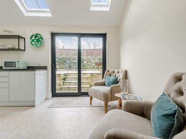 A kitchen area with a microwave and two armchairs with blue cushions near sliding glass doors at Wall Cottage in Burford