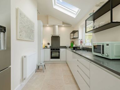 A kitchen with white cabinets a skylight and a mint green microwave at Wall Cottage in Burford