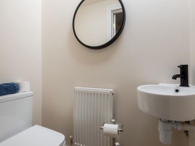 A small bathroom with a toilet towel and toilet paper a round mirror a radiator and a sink with a black faucet at Wall Cottage in Burford