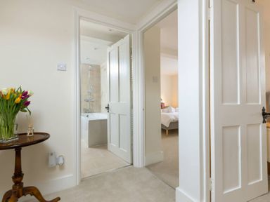 A hallway with doors leading to a bathroom and bedroom with a table holding flowers at Wall Cottage in Burford