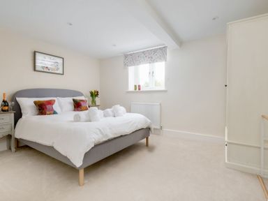 A bedroom with a grey bed and white bedding with colorful pillows and rolled towels at Wall Cottage in Burford