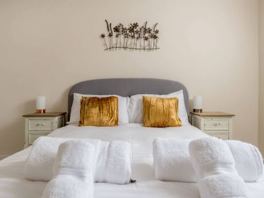 A bedroom with a bed with white linens golden pillows and rolled white towels at Wall Cottage in Burford