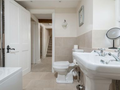 A bathroom with a toilet a sink a mirror and an open door showing a hallway and stairs at Wall Cottage in Burford