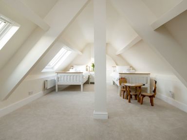 An attic bedroom with two beds under slanted ceilings and a small wooden table with chairs at Wall Cottage in Burford