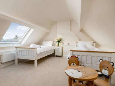 A bedroom with two single beds a small table with bear designs and a slanted window at Wall Cottage Burford