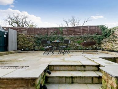 An outdoor patio area with stone steps a table with chairs a fire pit and a stone wall at Wall Cottage in Burford