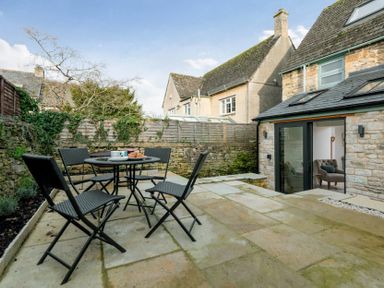 An outdoor patio area with a black table and chairs set and stone walls surrounding it at Wall Cottage in Burford