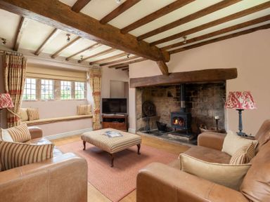 A living room with exposed wooden beams a wood stove leather sofas and a window seat at Little Gables in Broadway