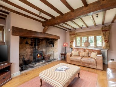 A living room with a wood burning stove stone fireplace leather sofas striped ottoman and wooden beams on the ceiling at Little Gables Broadway