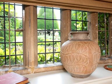 A large decorated ceramic vase on a window sill with a garden visible through black grid windows at Little Gables in Broadway