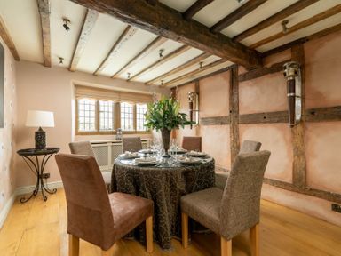 A dining room with a round table set for six and wooden beams on the ceiling and walls at Little Gables in Broadway