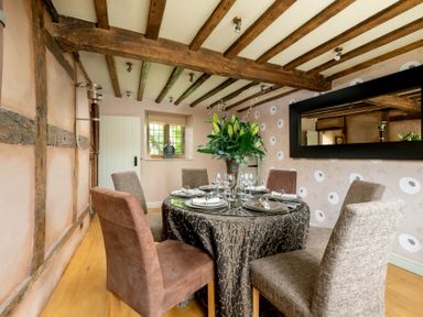 A dining room with a round table set for six with chairs and flowers on the table at Little Gables in Broadway