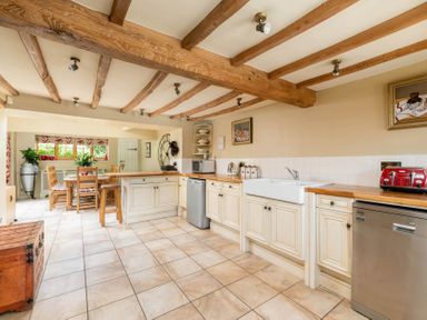 A kitchen with wooden beams on ceiling cream cabinets tiled floor and a dining table with chairs at Little Gables Broadway
