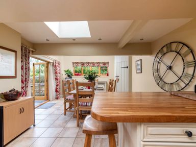 A dining area with wooden table and chairs a large wall clock and a wooden counter at Little Gables in Broadway