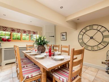 A dining room with a wooden table set for six and a large wall clock at Little Gables in Broadway
