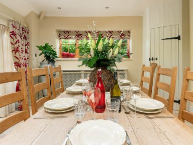 A dining room with a wooden table set with plates glasses and bottles and a flower centerpiece at Little Gables in Broadway