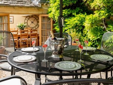 An outdoor dining table with plates and glasses containing strawberries and a bottle in an ice bucket at Little Gables in Broadway