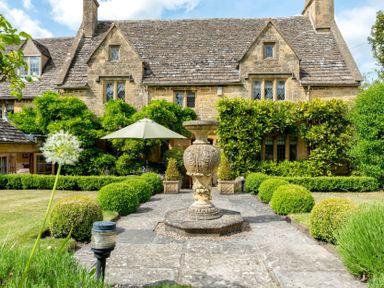 A stone house with hedges and an umbrella in the garden at Little Gables in Broadway