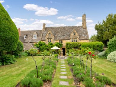 A garden with a stone pathway and small plants leading to a stone house with a tiled roof at Little Gables in Broadway