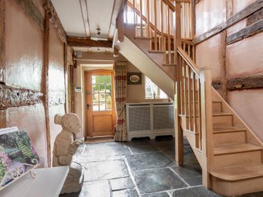 An entryway with wooden stairs stone floor a wooden door and a statue at Little Gables in Broadway