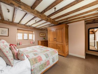 A bedroom with a bed covered in a quilt and pillows a wooden wardrobe a wooden dresser and a mirror at Little Gables in Broadway