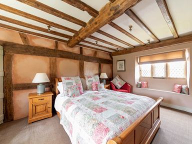 A bedroom with wooden bed frame quilted bedspread wooden nightstands lamps exposed wooden ceiling beams and a window seat at Little Gables in Broadway