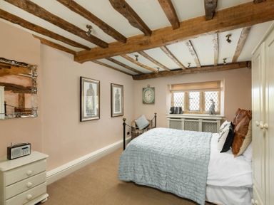 A bedroom with wooden beams on the ceiling a bed a chair a window and a small dresser at Little Gables in Broadway