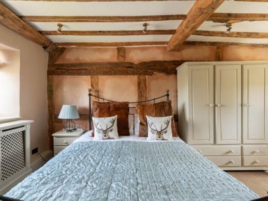 A bedroom with a bed with animal print pillows a nightstand with a lamp and a wardrobe at Little Gables in Broadway
