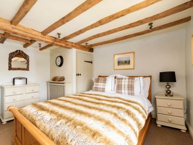 A bedroom with a wooden bed with striped blanket two nightstands a lamp a dresser a mirror and wooden ceiling beams at Little Gables Broadway