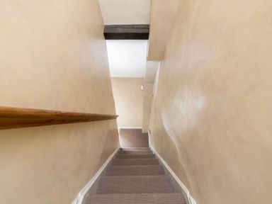 A narrow stairway with carpeted steps and wooden handrail descending to a lower level at Little Gables in Broadway