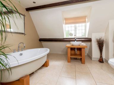 A bathroom with a bathtub wooden sink stand a window and a dried plant at Little Gables in Broadway