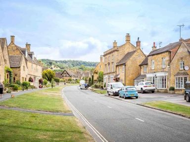 A street with parked cars and stone houses with chimneys and a grassy verge at Little Gables in Broadway