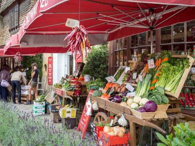 An outdoor market stall with vegetables and herbs under a red awning at Little Gables in Broadway