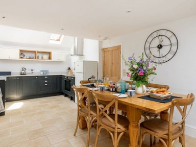 A kitchen with dark cabinets and a wooden dining table with chairs and flowers at Copperbeech in Stow-on-the-Wold