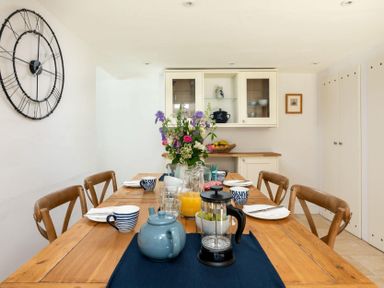 A dining room with a wooden table set with cups plates utensils a teapot a French press and flowers at Copperbeech in Stow-on-the-Wold