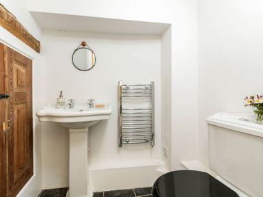 A bathroom with a pedestal sink mirror heated towel rack near a wooden door and toilet at Copperbeech in Stow-on-the-Wold