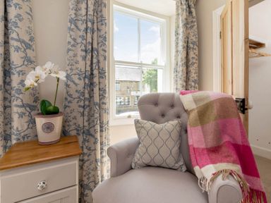 A corner with an armchair next to a window and a side table with a potted plant at Copperbeech in Stow-on-the-Wold