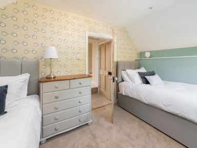 A bedroom with two single beds a chest of drawers a table lamp and bicycle patterned wallpaper at Copperbeech in Stow-on-the-Wold