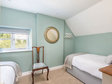 A bedroom with two single beds a wooden chair a round mirror and a window at Copperbeech in Stow-on-the-Wold