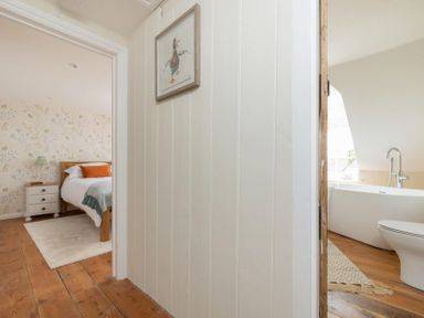 A view of a bedroom with a bed and nightstand and a bathroom with a bathtub and toilet at Copperbeech in Stow-on-the-Wold