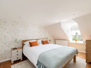 A bedroom with a wooden bed white bedding and orange pillows at Copperbeech in Stow-on-the-Wold