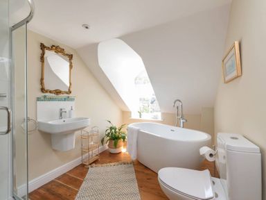 A bathroom with a bathtub near a window a toilet a sink with a mirror and a shower at Copperbeech in Stow-on-the-Wold