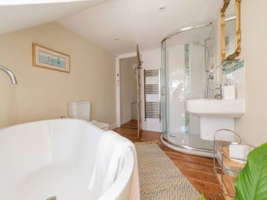 A bathroom with a bathtub toilet shower sink mirror and wooden flooring at Copperbeech in Stow-on-the-Wold