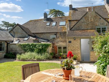 A garden with wooden table and chairs and stone houses in the background at Copperbeech in Stow-on-the-Wold