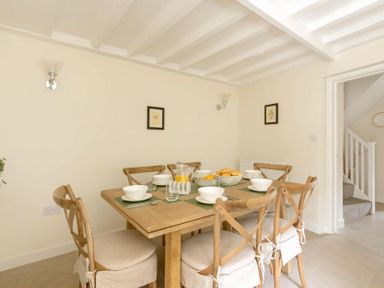 A dining room with a wooden table set with bowls and glasses and six chairs at Holly Cottage Middle Tysoe in Tysoe