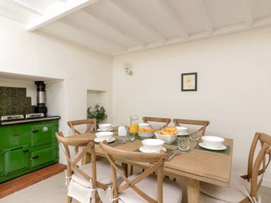 A dining room with a wooden table set with bowls glasses and cutlery next to a green stove at Holly Cottage Middle Tysoe in Tysoe