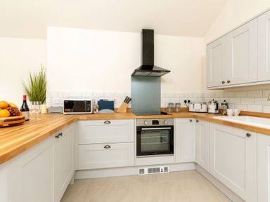 A kitchen with wooden countertops white cabinets a stove microwave toaster and fruit bowl at Holly Cottage Middle Tysoe in Tysoe
