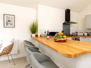 A kitchen with a wooden countertop bar and gray chairs and a fruit bowl at Holly Cottage Middle Tysoe in Tysoe